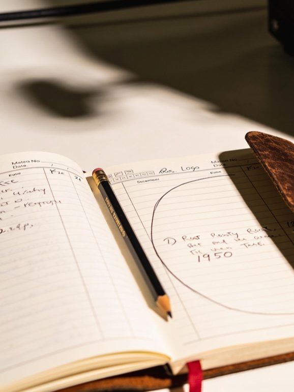 Opengeslagen logboek met handgeschreven aantekeningen en een getekende brandcurve, met een potlood tussen de pagina's.